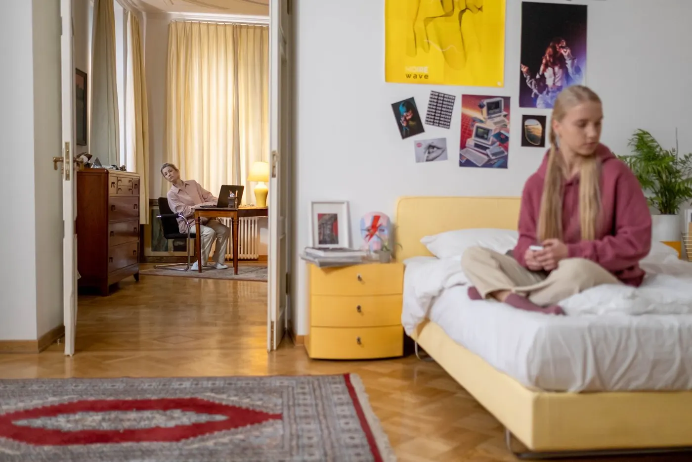 Un'adolescente seduta sul letto nella sua stanza, il genitore lontano nell'altra